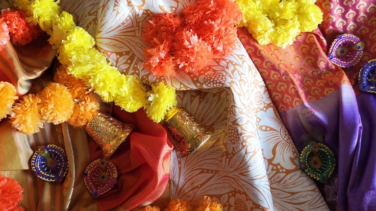 Cream and orange silk sari fabric lies on the floor draped with orange and yellow marigold garlands
